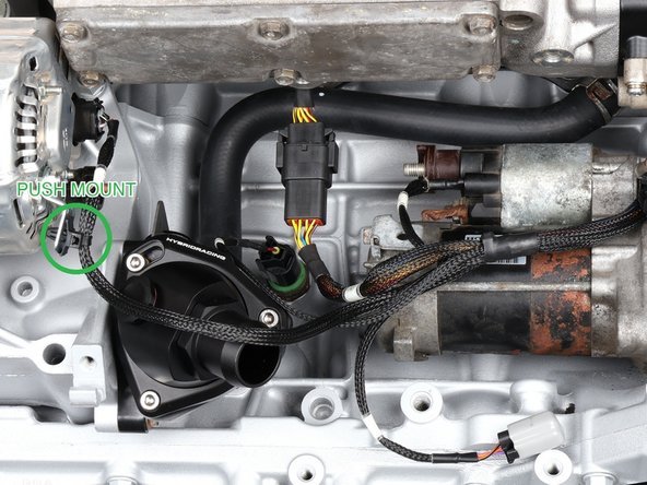 Zip tie the harness along the engine using the included push mounts in the OEM harness holes: two on the back side by the VTS and VTC solenoids, one by the starter, one at the alternator (green ring, marked PUSH MOUNT), extras where your build needs them. Leave the ties loose until the cabin section reaches the ECU in Step 11, then tighten.