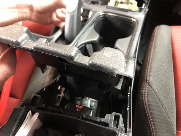 Open the center console storage compartment and use a plastic trim tool to pop the cup-holder section up. Start on the edges and pull upwards while prying. It will pop loose and expose the shifter and e-brake assembly.