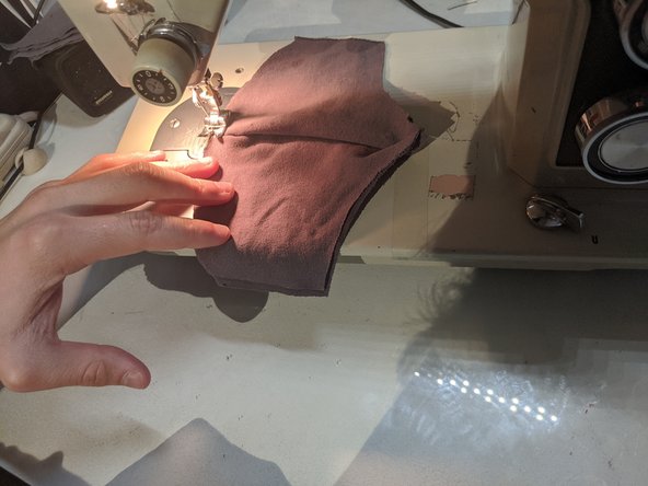 Unfold your mask so you have two layers of cloth on either side. Start sewing along the outline of the mask, but stop about an inch away from the sides. Turn 90 degrees and sew to the other side. Continue until you have sewn the entire outline, then cut your string and tie the loose ends.