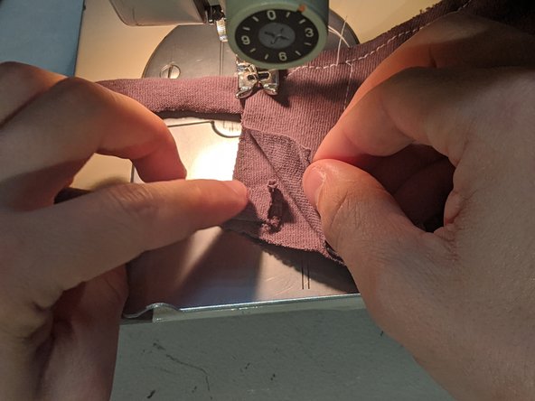 Sew down until you are about an inch away from the bottom and place the bottom strap between your two layers. Sew across it to the bottom and then turn the mask 90 degrees.