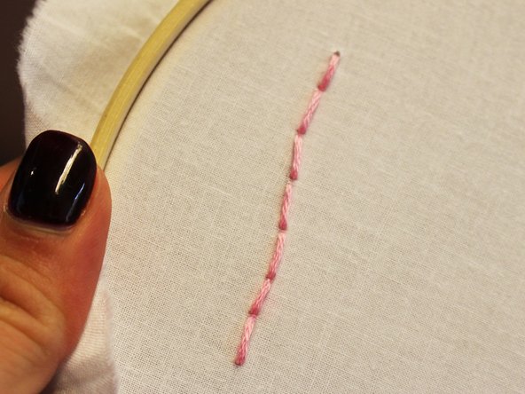 From the back, pull the needle and thread up through the fabric starting a bit ahead of the beginning of the drawn line