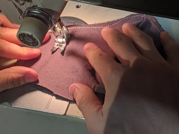 Unfold your mask so you have two layers of cloth on either side. Start sewing along the outline of the mask, but stop about an inch away from the sides. Turn 90 degrees and sew to the other side. Continue until you have sewn the entire outline, then cut your string and tie the loose ends.