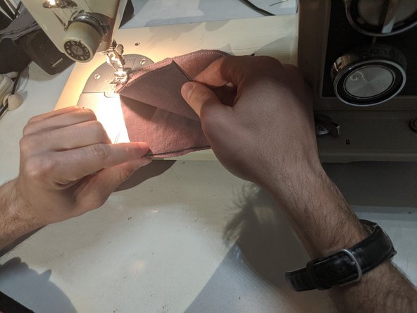 Unfold your mask so you have two layers of cloth on either side. Start sewing along the outline of the mask, but stop about an inch away from the sides. Turn 90 degrees and sew to the other side. Continue until you have sewn the entire outline, then cut your string and tie the loose ends.