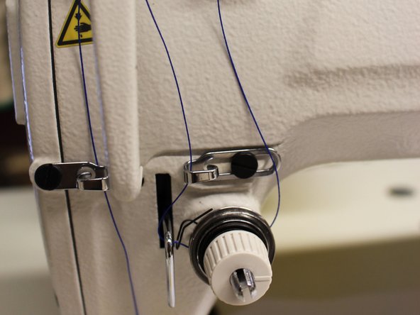 Now you'll want to wrap the thread around the bottom of the thread tension knob, and up through both metal levers next to the tension knob.