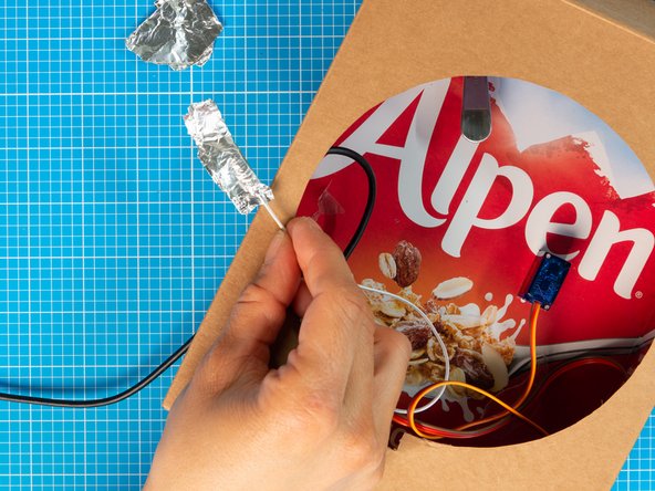 Wrap the metal on the end of the capacitive touch lead with a bit of aluminium foil. This will increase the  surface contact between the metal end of the lead and the spoon.