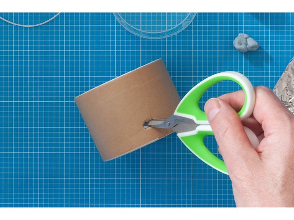 Mark a point towards the bottom of the container. In this example the hole is being created on the opposite side from the hole made for the button.