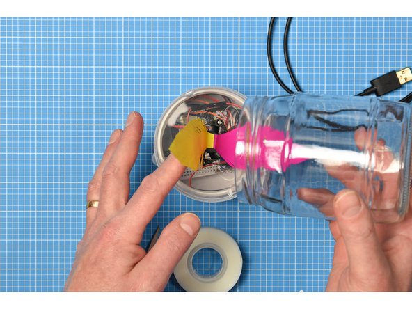 Place the pickle jar upside down onto the assembly. You will need to hold up the feathers and tuck them inside the jar. The jar itself will sit neatly inside the upturned cotton bud lid, but you may wish to secure it with extra tape.