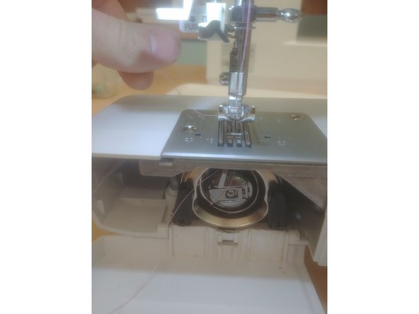 Pull the thread left through the hook (set in a groove) at the top of the machine, then pull towards yourself.