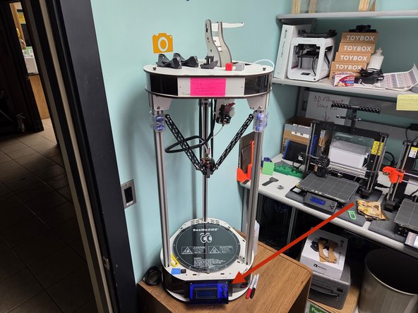 The Rostock Max V2 can be identified by its large vertical size and white coloration. Its control panel is located near the bottom of the machine.