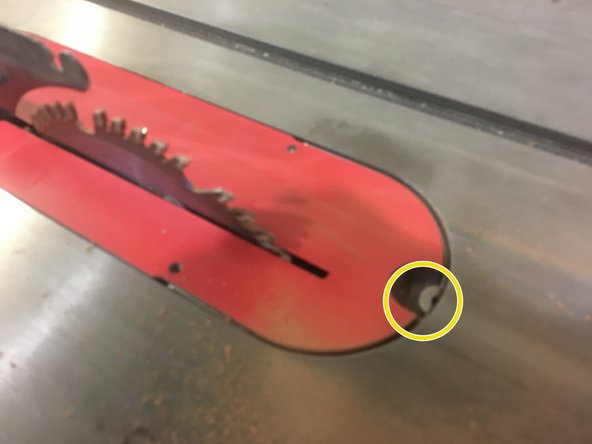 Locate the metal tab on the front of the throat plate.