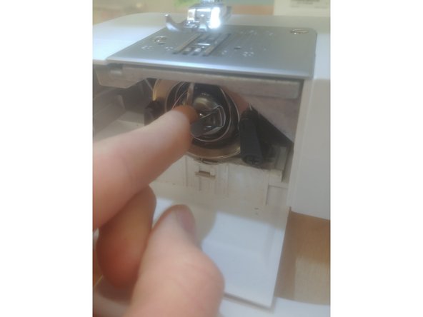 Slide out the case at the bottom of the machine by pulling it to the left. Open the small door directly below the needle by pulling forward.