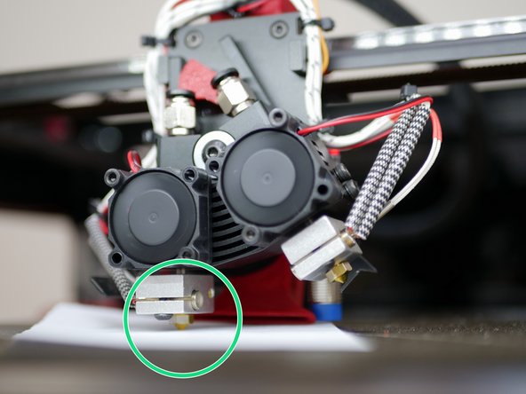 Loosen the bolts holding the second heater block and lower it down until the piece of paper is trapped between the nozzle and bed.