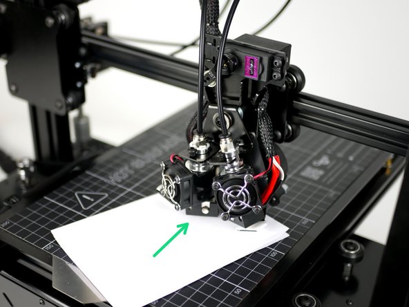 Take the folded piece of paper and place it between the surface and the nozzle of Hotend #1.