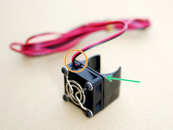 Assemble the fan with the sticker facing inwards and the fans cable coming out of the top left like shown in the third image.