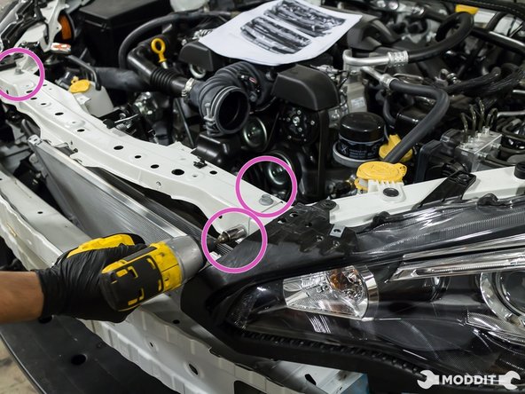 With a preferred racheting 12mm wrench, remove the two bolts securing the radiator support center brace to the lower radiator core support.