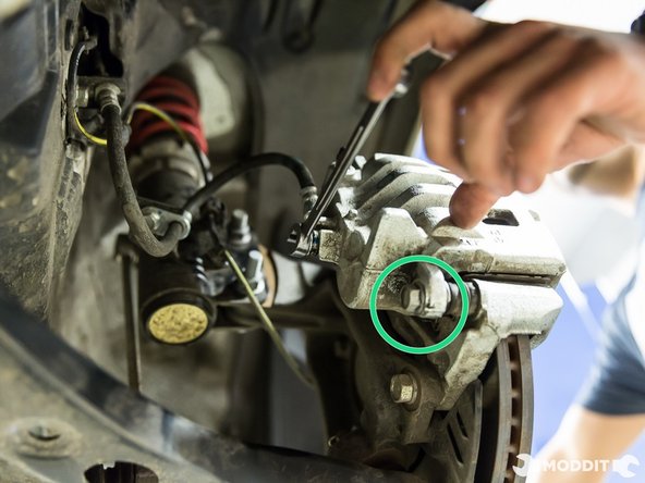 With a 14 mm wrench, remove the upper and lower bolt securing caliper to caliper bracket.