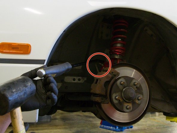 Image 3: The brake cable is attached to the car by a metal clip, use a pry bar or needle nose pliers to remove the clip.