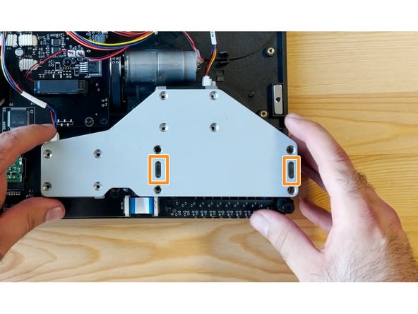 Once the screws are half tightened, you should see a small acrylic end from the two CAM caps, and two holes on the bracket. Gently position and push the bracket over these acrylic ends, before re-inserting the remaining silver screws to hold them in place. 