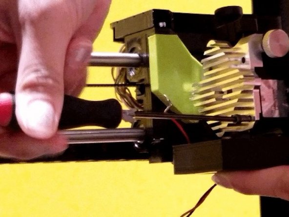 Re-install the cooling fan assembly with bottom left and bottom right bolt of heat sink. Start with bottom-right to secure cooling assembly. Press it upwards against the hot end assembly. Screw in bottom-left to also secure the cooling assembly. Nextscrew top-left with the red wire, using the shortest of the our screws.