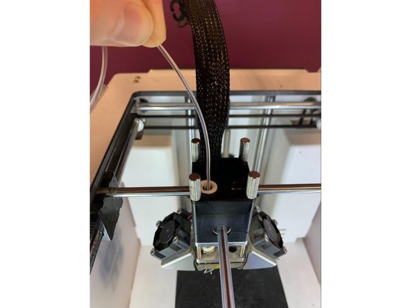Find 20-30cm of clear or white PLA. Manually press this down into the print core from the top of the print head until you have purged any remaining material which was in the print head. You should only see clear filament coming from the nozzle when it has been fully purged. Pull the filament you just inserted back out before proceeding .