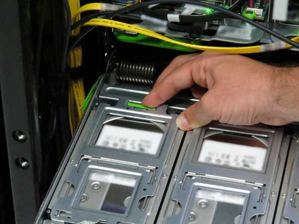 Press the green retention tab on the hard disk drive cage.