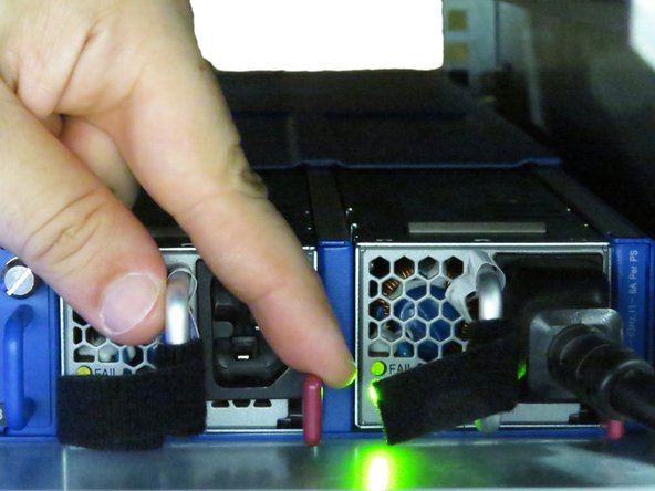 Press the red PSU retention tab towards the PSU handle, as shown.