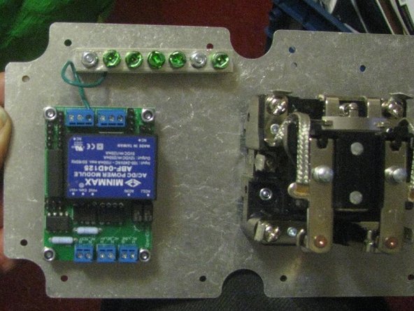 Orient the  metal base plate. The plate is drilled for more than one style of relay and board; not all the holes are used. The mounting holes for the ground bar may be identified (silver nuts here).