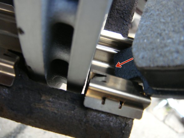 Glisser la nouvelle plaquette sur son ressort en commençant par le bas puis finir en la guidant en haut