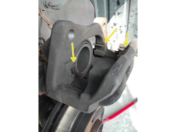 Si vous n'avez pas de gouttières neuves, nettoyer les 4 gouttières en métal (flèches jaunes) qui permettent le coulissement des plaquettes dans l'étrier. Seulement 3 sont visibles sur la photo.