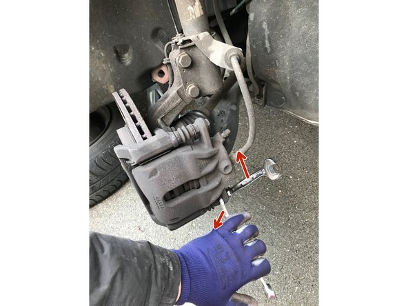 Dévisser la vis inférieure de maintien de l'étrier avec une clé de 13 tout en maintenant le coulisseau avec une clé de 15