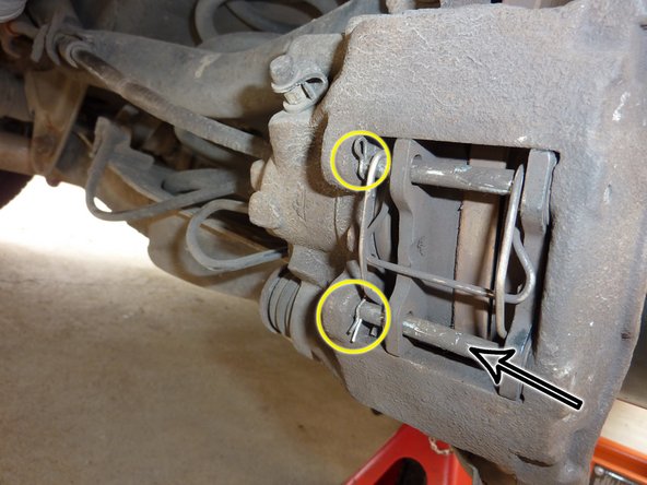 Appuyer sur le ressort afin de le mettre contre les plaquettes de frein et remonter la goupille du bas (flèche noire).