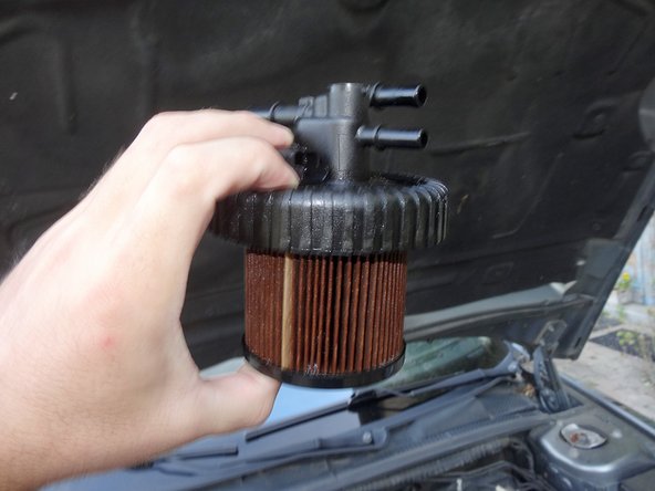 Soulevez délicatement le couvercle, le filtre est fixé en dessous et doit donc venir avec. Laissez le s’égoutter ou prévoyez un chiffon ou du papier essuie tout afin de ne pas mettre du carburant partout en vous éloignant.