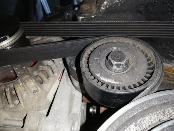 Repérer le galet tendeur. A l'aide d'une clé à cliquet avec une douille de 15, tourner la clé dans le sens horaire. Le galet va bouger et détendre la courroie.