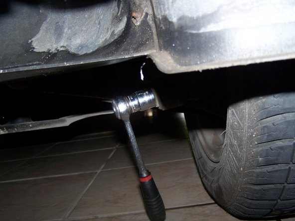 Sous la voiture, utiliser la clé de 18 pour dévisser le pied de l'amortisseur