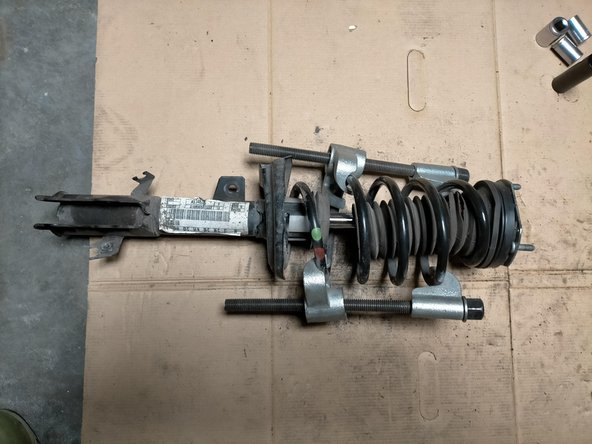 Comprimer le ressort avec un matériel approprié jusqu'à libérer les coupelles de la pression.