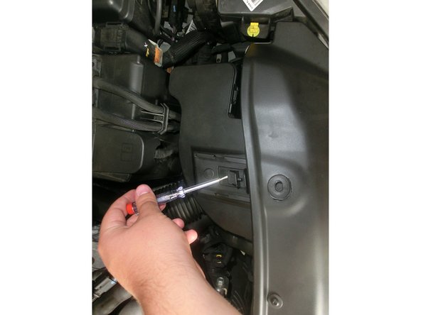 Enlever ensuite le résonateur d'air pour cela glisser un tournevis sous l'encoche et relever la tout en la tirant vers le moteur. Le résonateur est alors désolidariser de la calandre.