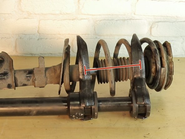 Placer l'amortisseur sur l'établi, puis installer le compresseur de ressort sur les spires les plus proches de l’extrémité