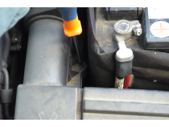 Avec le tournevis cruciforme modèle Phillips démonter le cache supérieur du filtre à air et une partie du tuyau d'air afin de le décaler vers la gauche. Cela permet d'avoir accès à la vis de 13 qui fixe la batterie à sa base.