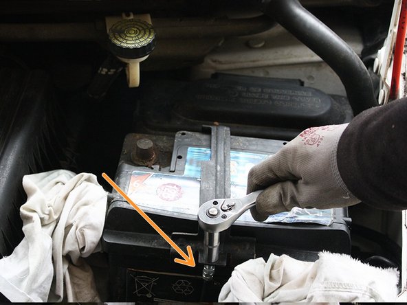 A l'aide d'une clé à cliquet avec douille de 10, dévisser les deux écrous qui retiennent la bride de fixation de batterie, récupérer les écrous en veillant à ne pas les faire tomber.