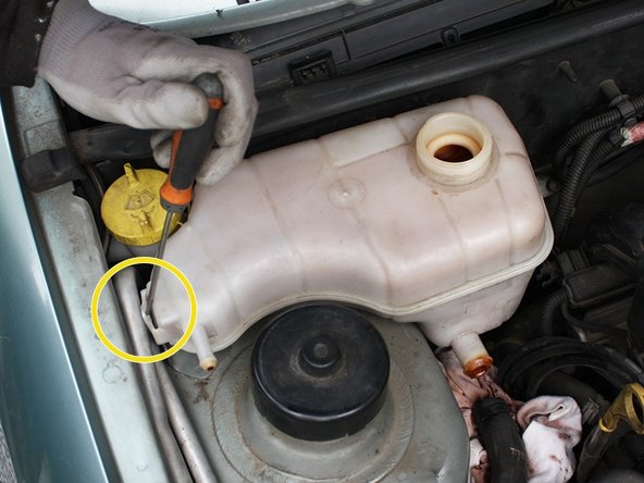 Avec un tournevis plat, faire levier sur la patte de support situé du coté de l'aile droite du véhicule afin de dégager le vase d'expansion.