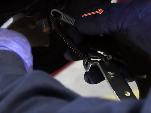 Desserrer le ressort du kit de frein puis le faire passer devant le câble de frein à main et le raccrocher