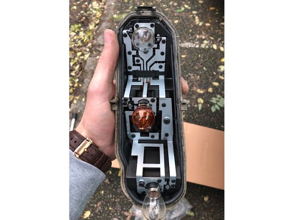 Enlever et récupérer le cercle de protection en mousse. Ensuite démonter le support des ampoules. Pour cela, il y a 2 ergots situés en haut et en bas de l'optique (voir cercles rouges sur la photo)