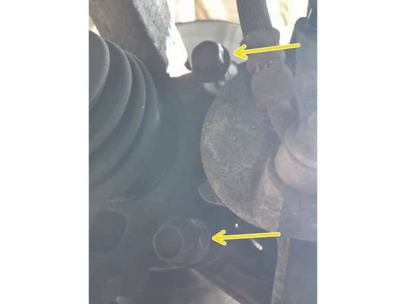 Derrière le disque, l'étrier est tenu par 2 boulons (flèches jaunes). Utiliser une clé de 17mm pour les dévisser totalement et les retirer du support. Attention, tenir l'étrier pour ne pas risquer de le faire tomber.