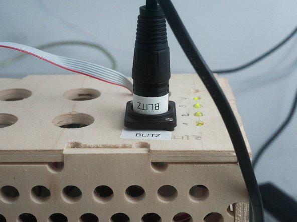 Das schwarze Blitzkabel nach unten ziehen und in der hellen Holzbox einstecken.