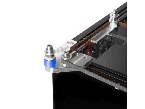 The belt should cross to the left of the printer, and the teeth should engage the toothed idler on the shorter, inside shoulder bolt on the rear idler mount.