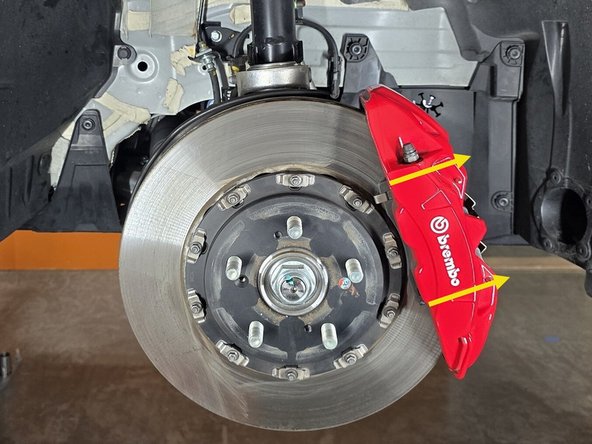 With the bolts removed, slide the brake caliper off the rotor in the direction of the yellow arrows