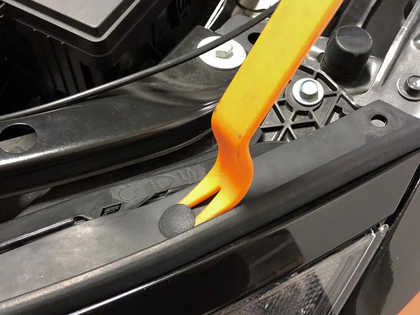 Starting on the driver's side, remove the five push clips that connect the hood weather stripping to the bumper using a flathead screwdriver or trim removal tool