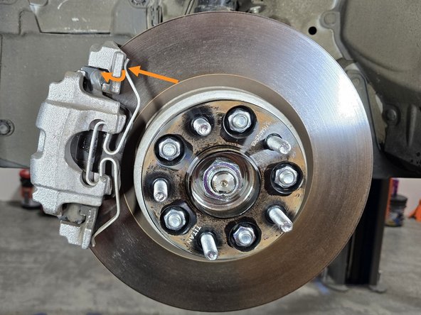 Using a flat head screw driver, pop the tension clip off of its perch on the top of the caliper