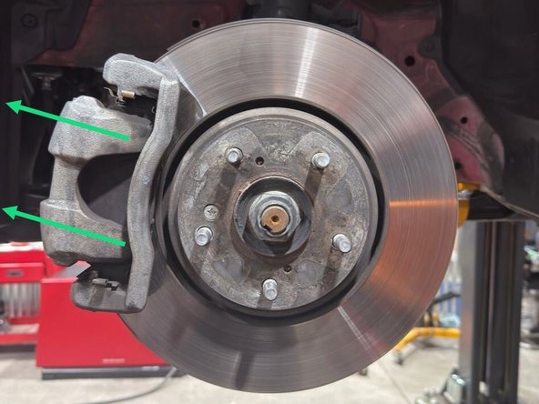 Using a 14mm socket and a 3/8" drive ratchet, remove the two caliper slider bolts circled in yellow