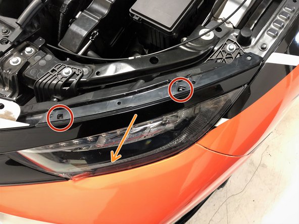 Using a small screwdriver, push down on the two tabs to release the upper headlight trim from the headlight on the driver's side